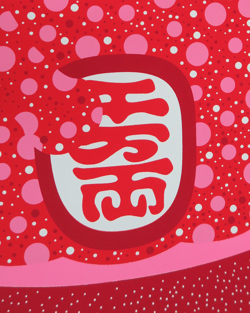 Close up of the lucky cat holding a medallion in red, pink and white dots.